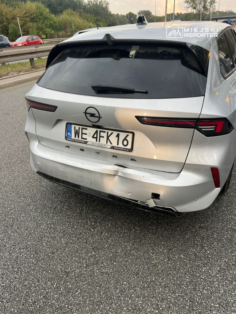 Uszkodzony tył srebrnego samochodu osobowego zaparkowanego na drodze, z widocznymi zarysowaniami i uszkodzeniami.