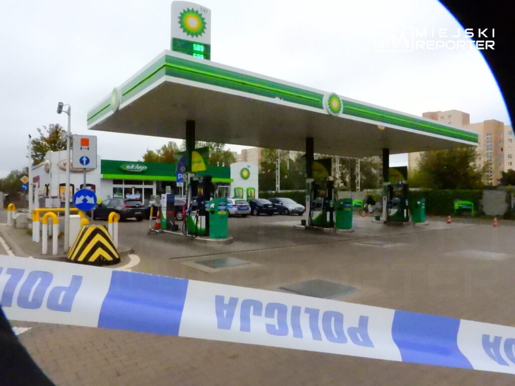 Stacja benzynowa BP z widocznymi dystrybutorami i sklepem, otoczona taśmą policyjną.