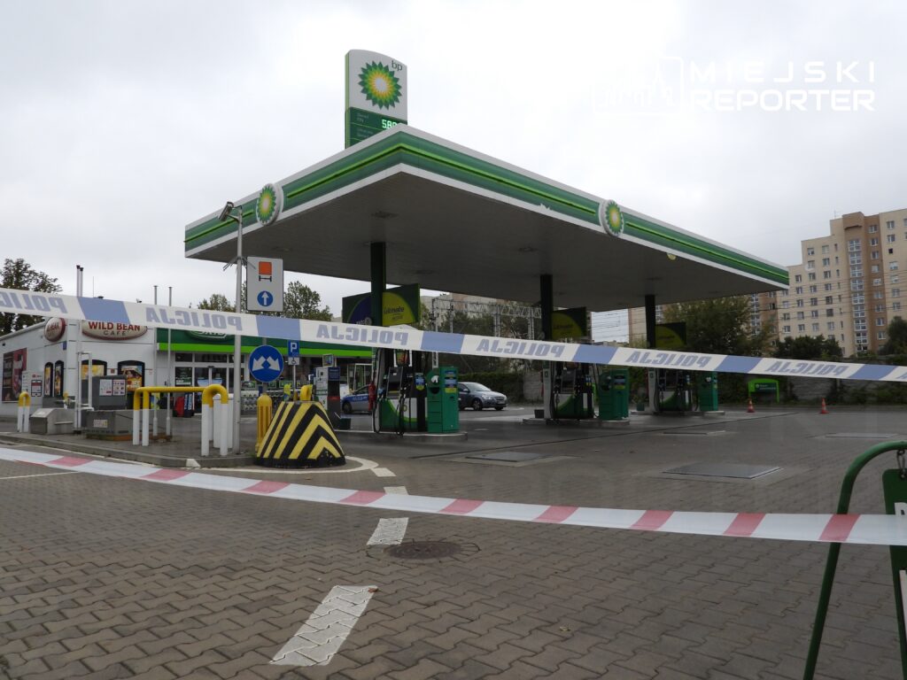 Stacja benzynowa z oznaczeniem BP, ogrodzona taśmą policyjną, w tle bloki mieszkalne.