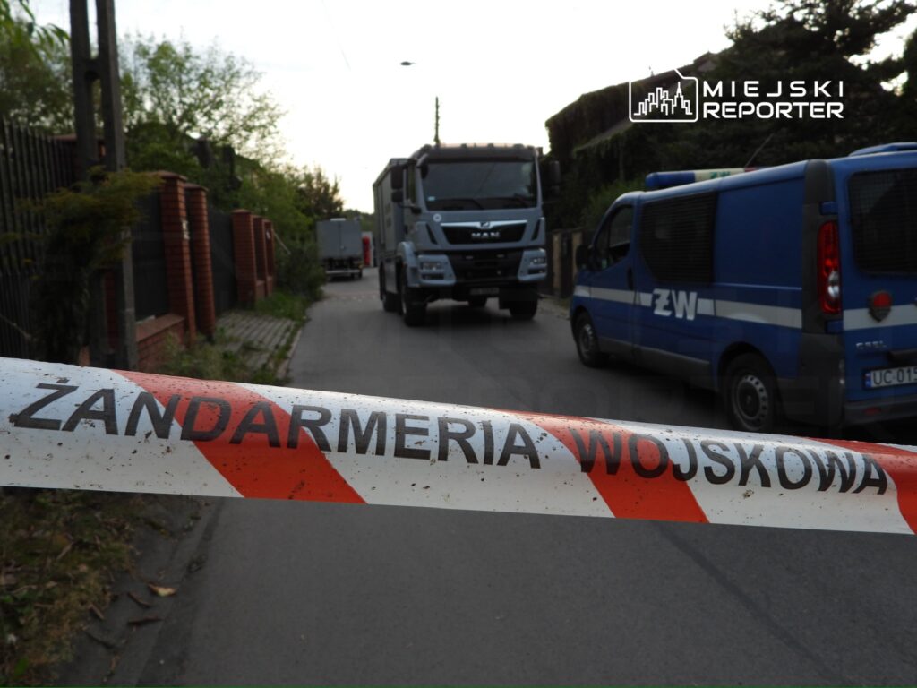 Wojskowy kordon z napisem „Żandarmaria Wojskowa” blokuje ulicę, a w tle widoczne pojazdy służb.