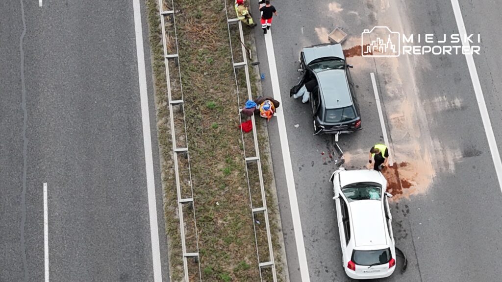 Wielu ratowników medycznych i strażaków udziela pomocy poszkodowanym na drodze po wypadku dwóch samochodów.