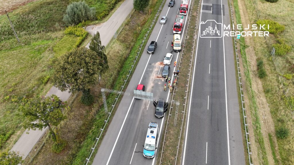 Na drodze krajowej zatrzymały się pojazdy, a strażacy oraz policjanci udzielają pomocy po wypadku.