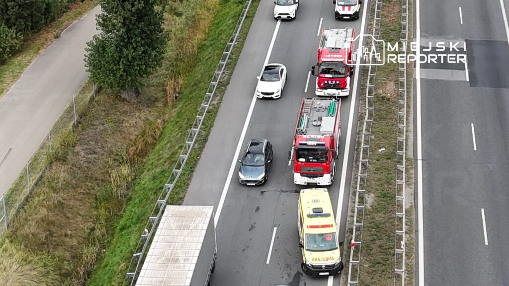 Ruch drogowy zablokowany przez pojazdy ratunkowe na autostradzie, obok widoczny pas zieleni i droga dla rowerów.