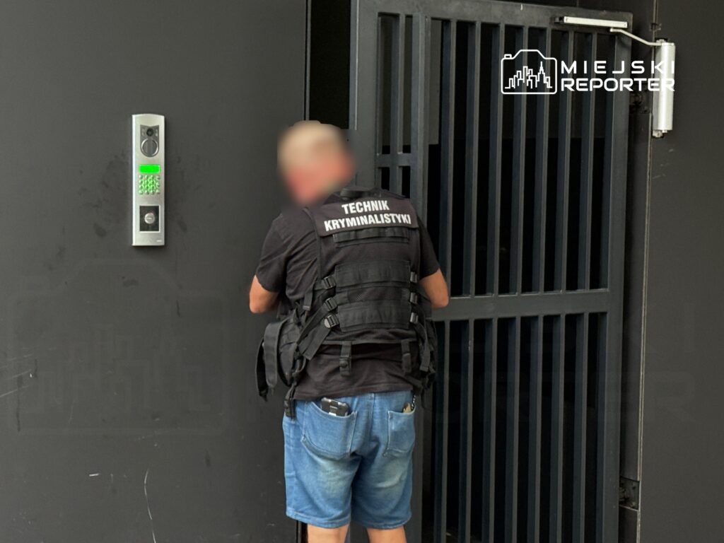 Technik kryminalistyki używa kodu dostępu do otwarcia metalowej bramy w miejskim otoczeniu.