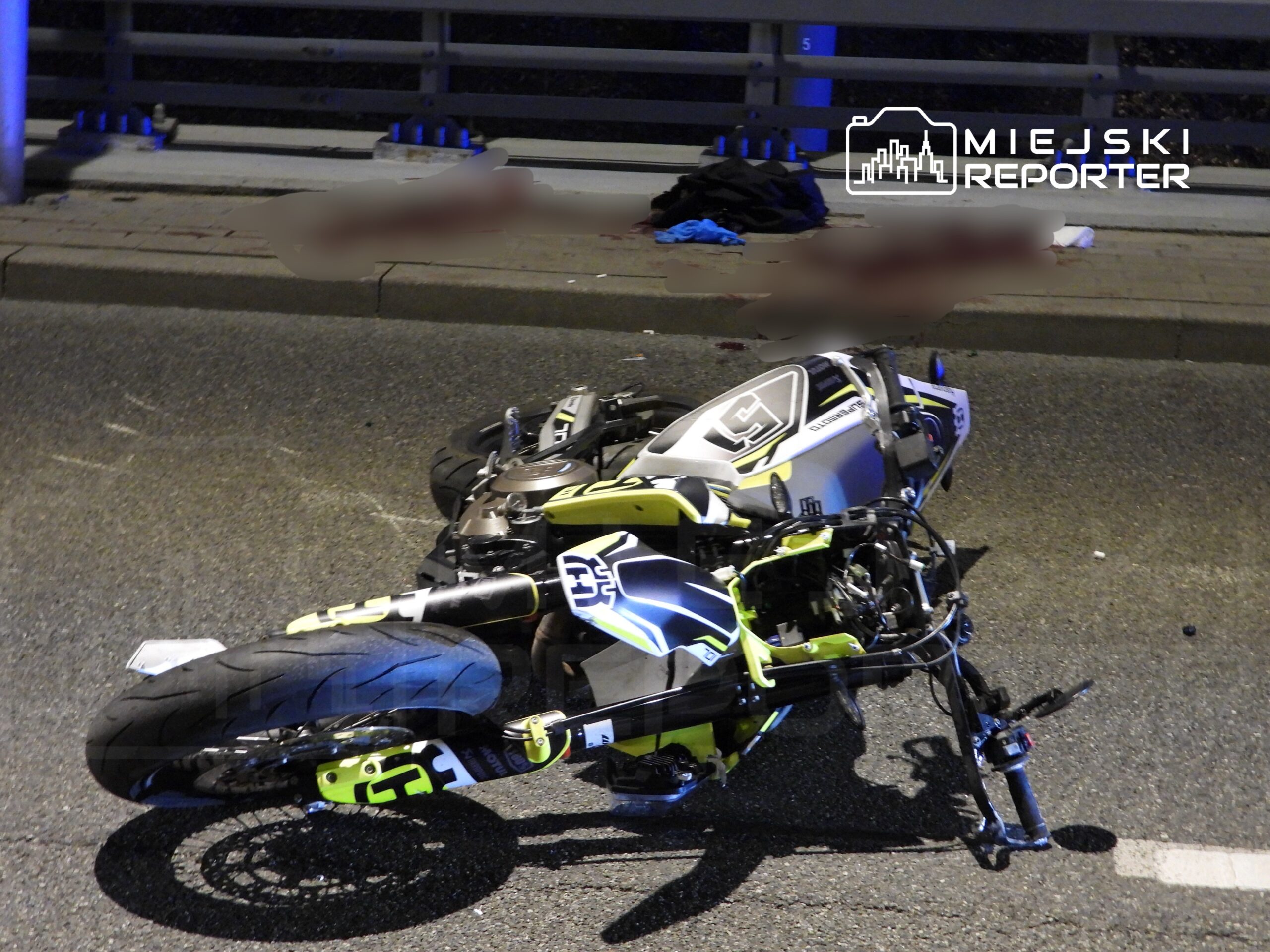 Motocykl leżący na drodze, z uszkodzeniem przedniego koła, obok widać porzucone ubrania. Nocna sceneria.