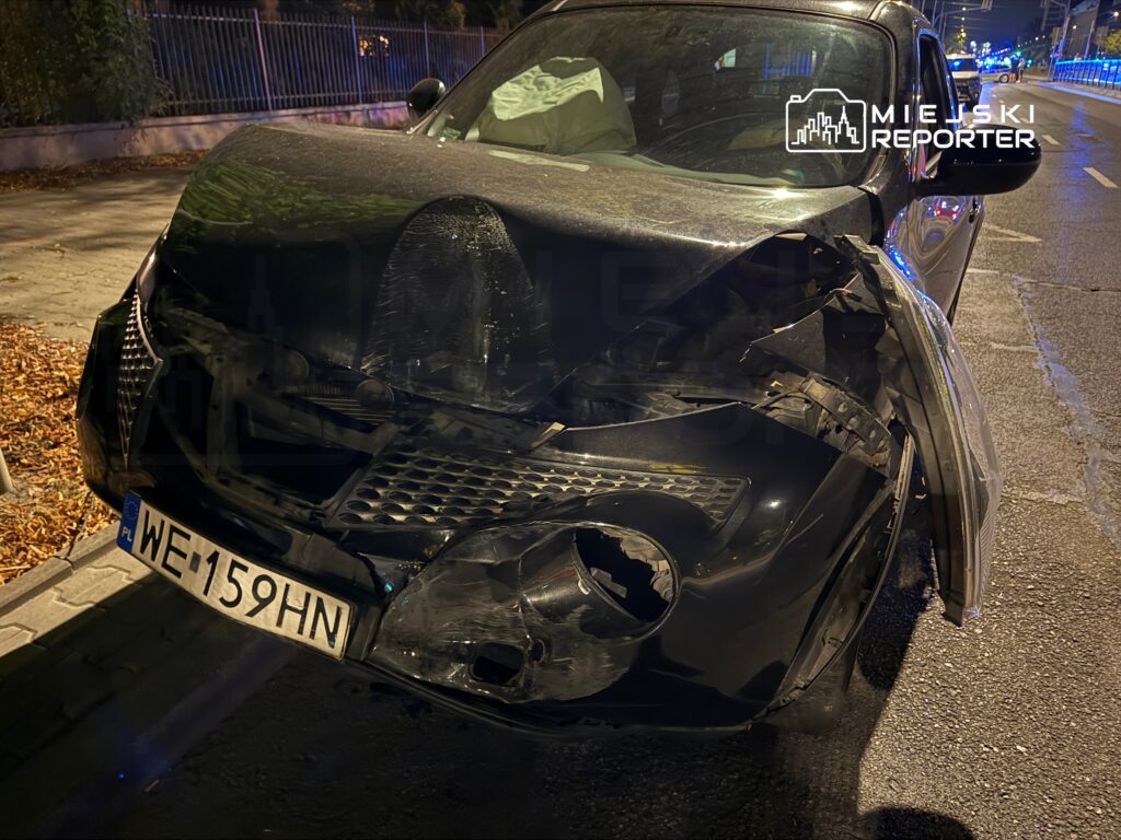 Uszkodzony czarny samochód osobowy z wgniecionym przodem stoi na ulicy, obok leżą liście.