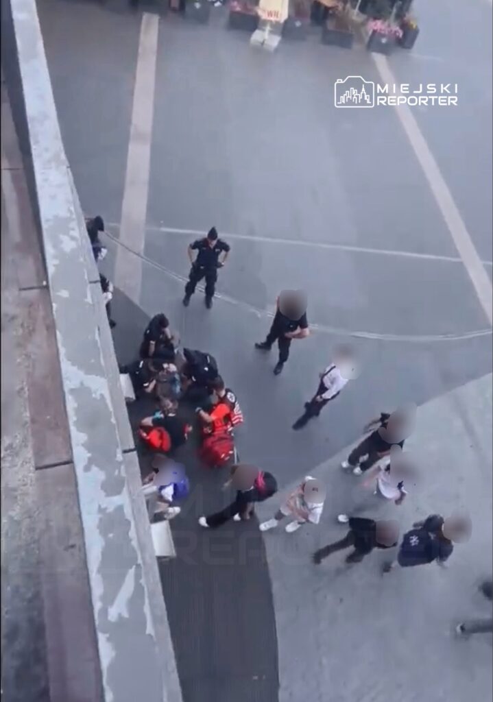 Grupa ratowników i policjantów udziela pomocy osobie leżącej na ziemi w miejskim otoczeniu.