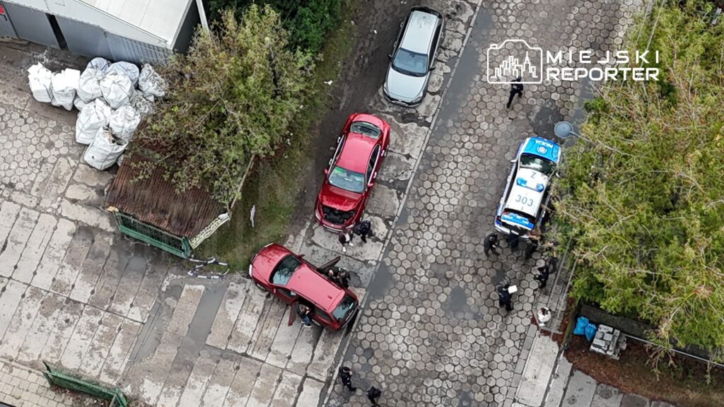 Czerwony samochód z otwartą maską stoi na ulicy, a obok grupka policjantów prowadzi czynności dochodzeniowe.
