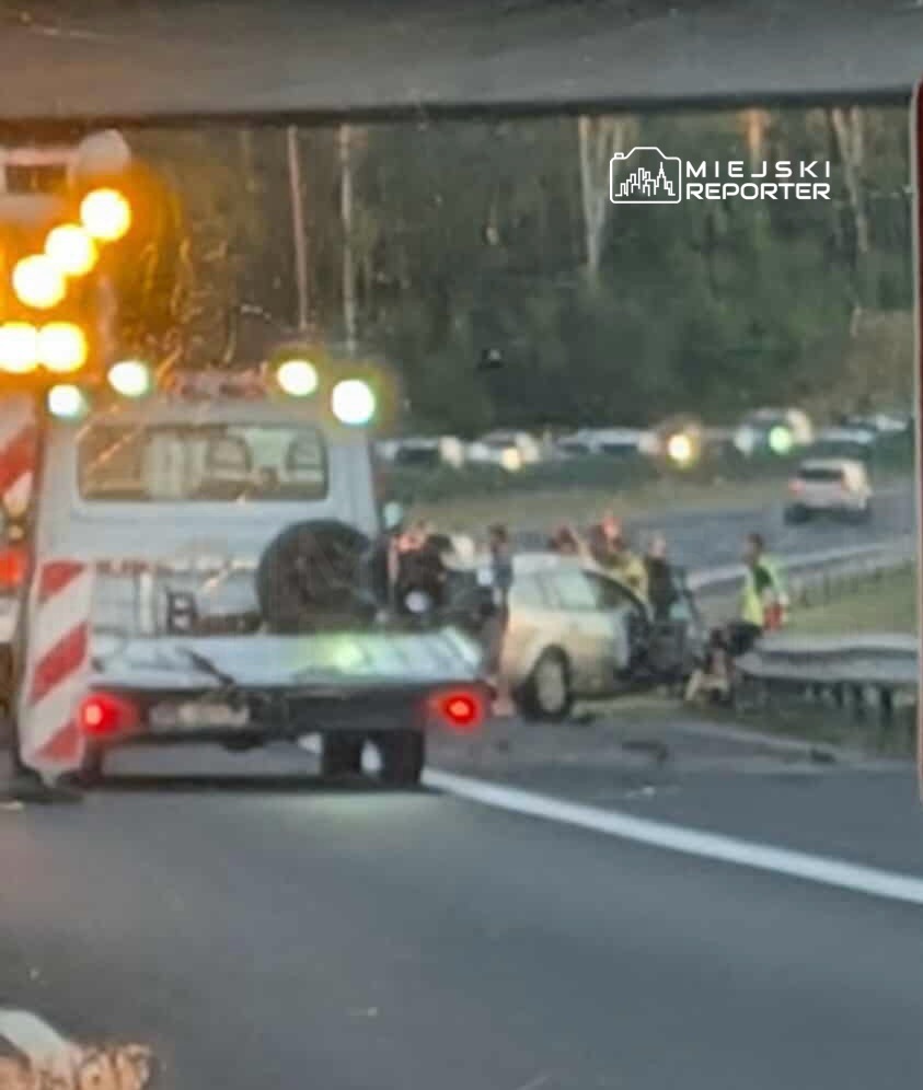 Wielu ludzi gromadzi się wokół miejsca wypadku drogowego na autostradzie, obok uszkodzonego pojazdu.