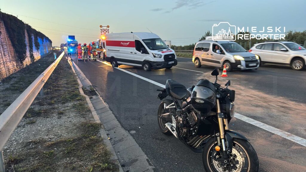 Na poboczu drogi stoi motocykl, obok zespół ratunkowy i pojazdy służb w trakcie interwencji.