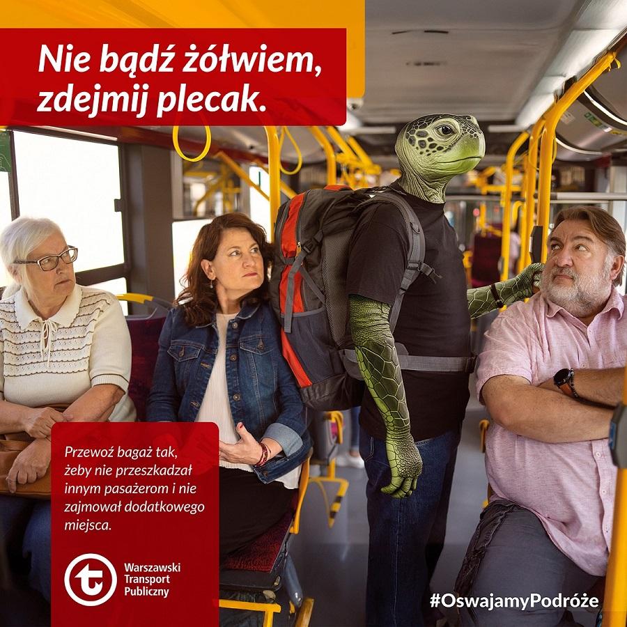 W autobusie mężczyzna w kostiumie żółwia stoi z plecakiem, a obok siedzą dwie kobiety i mężczyzna.