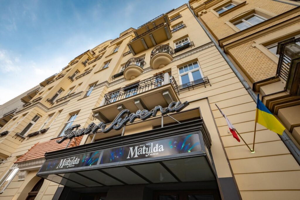 Budynek z przeszkloną fasadą i balkonami, z napisem "Teatr Syrena" oraz flagami Polski i Ukrainy.