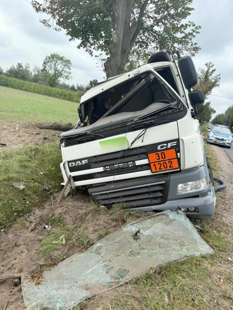 Ciągnik siodłowy DAF leży na boku przy drodze, obok zniszczona szyba i uszkodzone otoczenie.