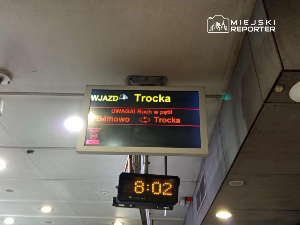 Tablica informacyjna na stacji pokazująca kierunek "Trocka" oraz ostrzeżenie o ruchu w pętli. Aktualny czas: 8:02.
