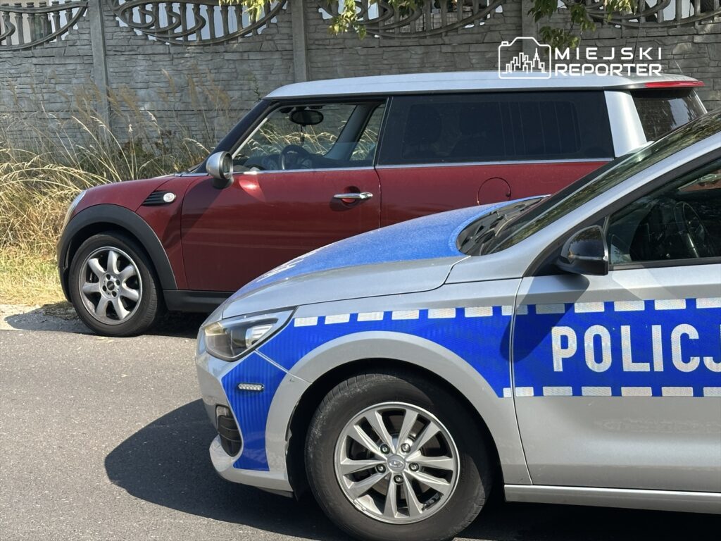 Czerwony samochód zaparkowany obok nieoznakowanego radiowozu policyjnego na asfaltowej drodze.