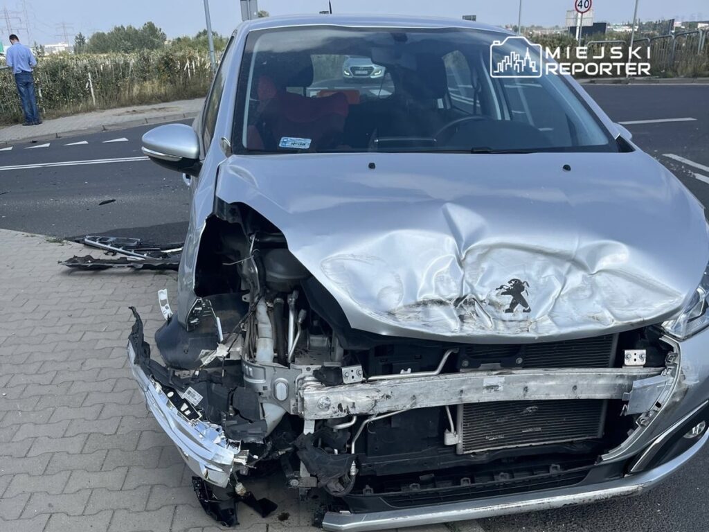 Uszkodzony samochód osobowy zaparkowany na chodniku, z widocznymi wgnieceniami na przedniej części i uszkodzoną atrapą.