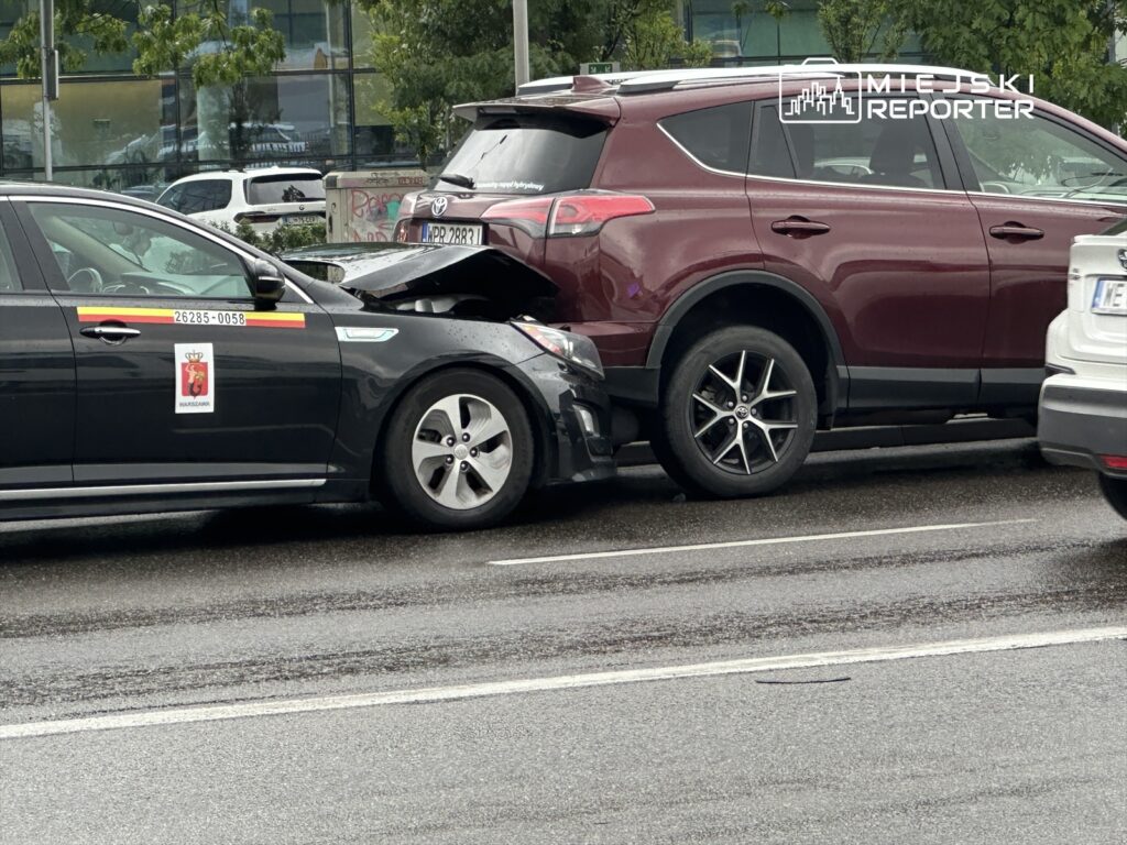 Czarny samochód osobowy z oznaczeniem taksówki zderzony z czerwonym SUV-em na miejskiej ulicy.