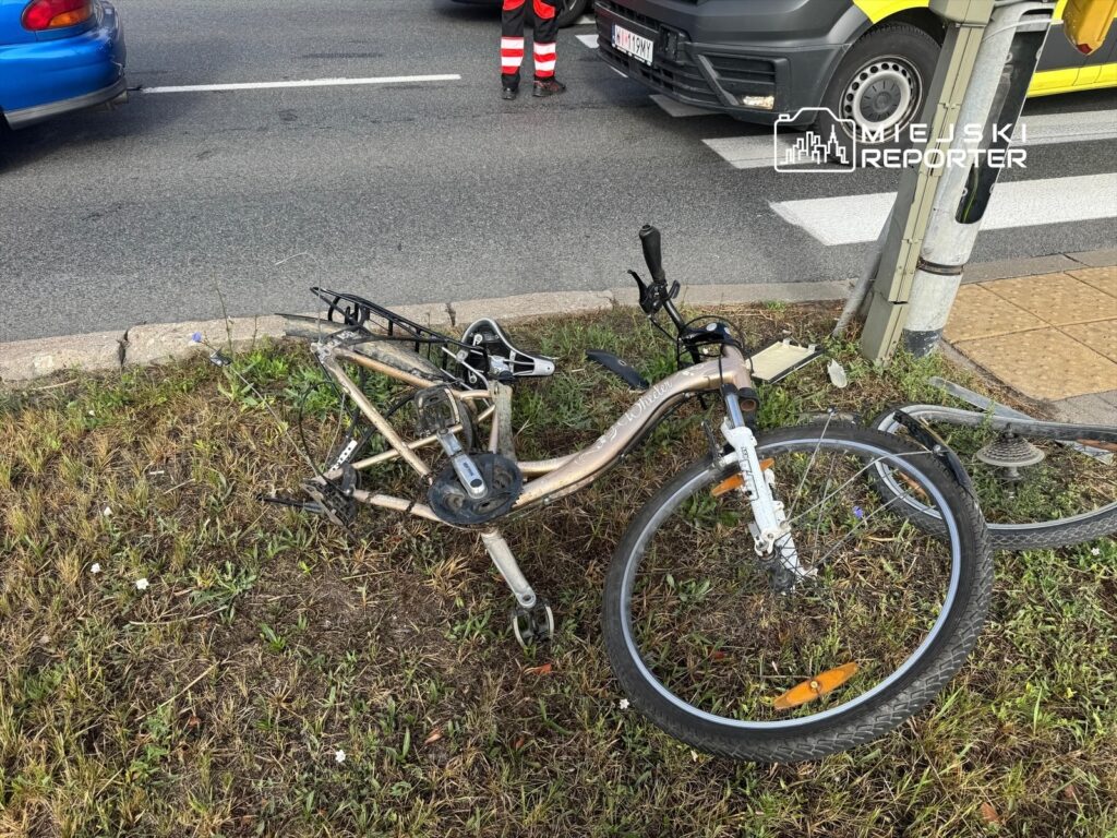 Zniszczony rower leży na trawie obok ruchliwej ulicy, obok przejścia dla pieszych.