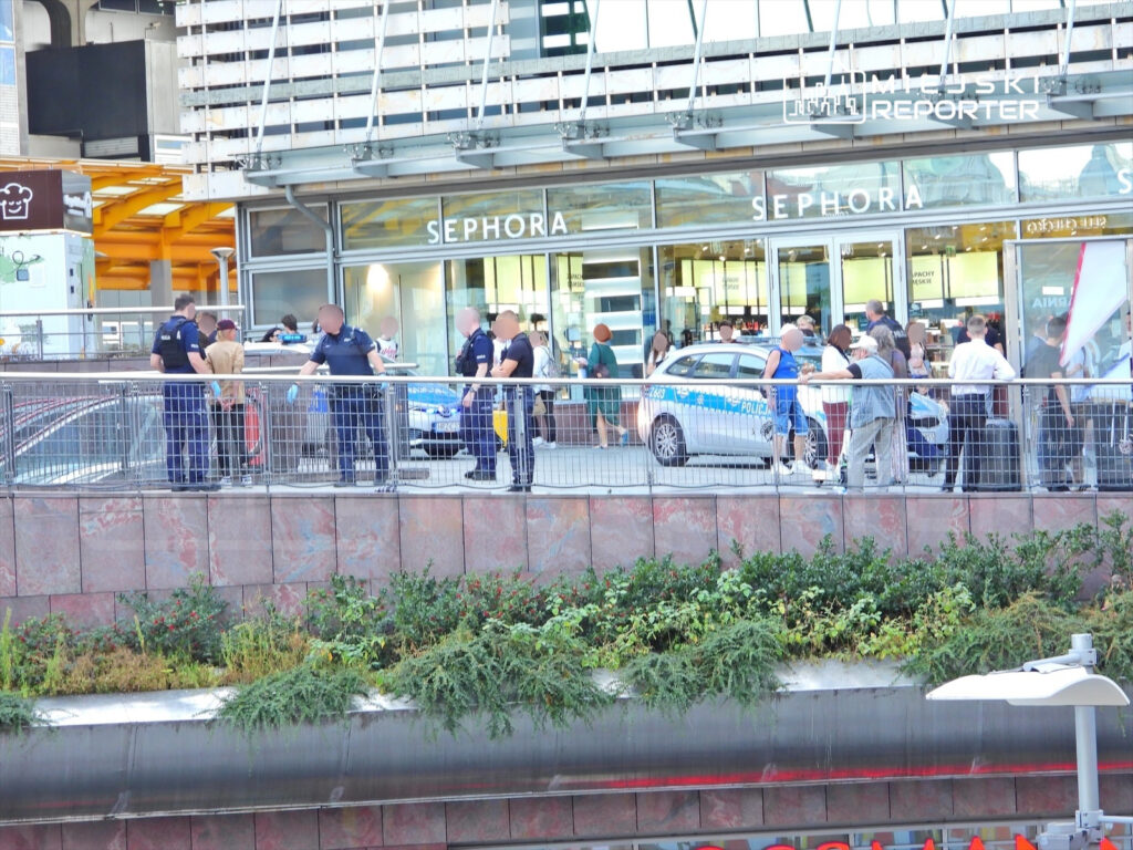 Grupa policjantów rozmawia z mężczyzną w beżowej koszuli w pobliżu sklepu Sephora, wokół zbiera się tłum ludzi.