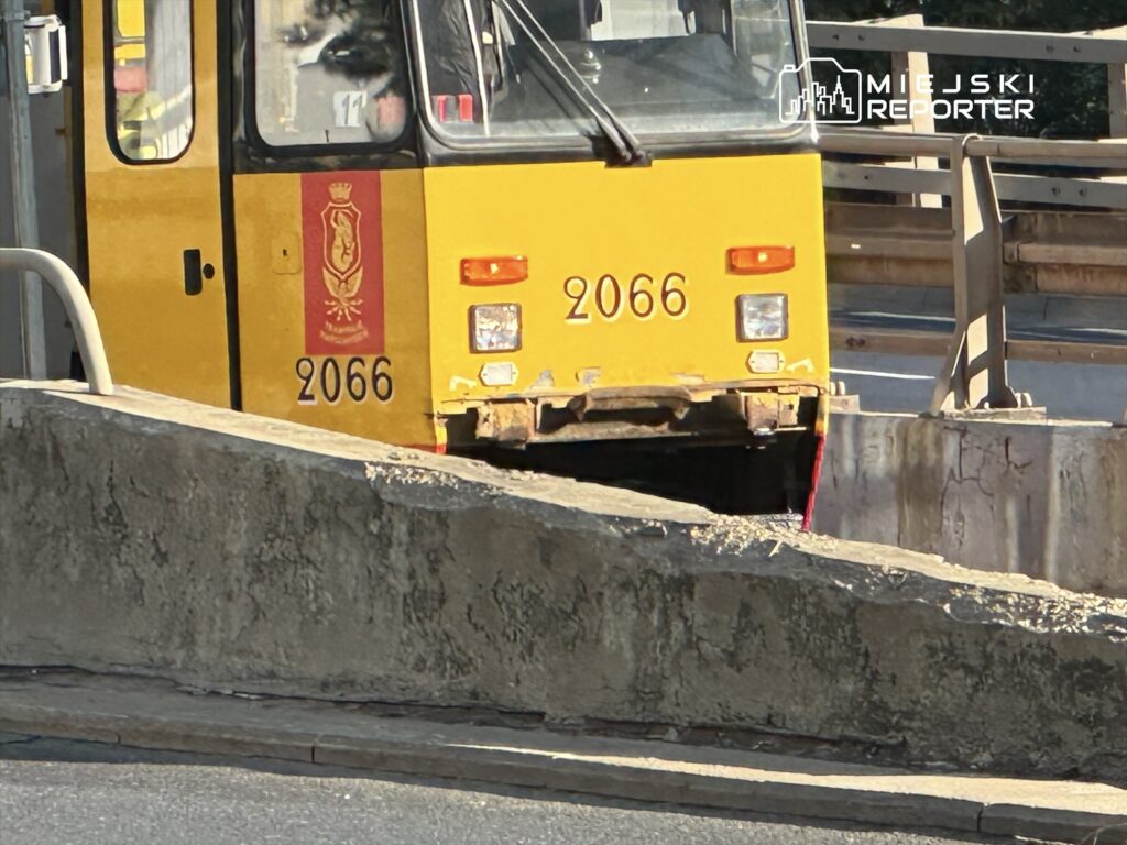 Żółty tramwaj z numerem 2066 zatrzymany na uszkodzonej trasie, z widoczną barierą betonową w tle.