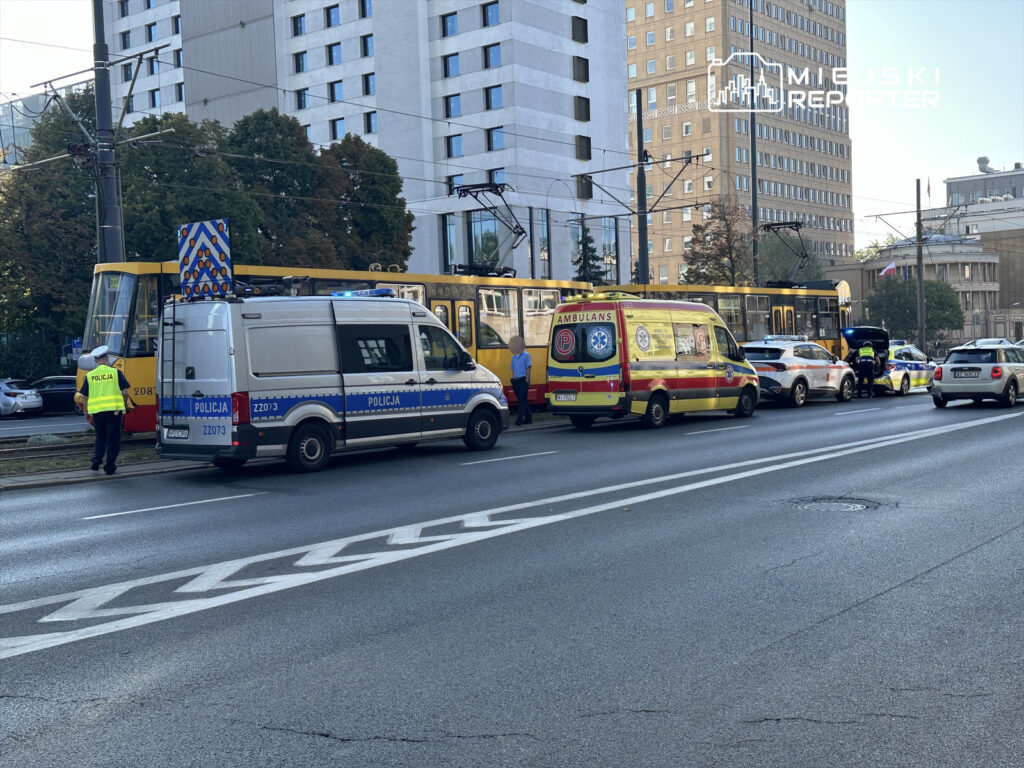 Policyjny radiowóz oraz karetka stoją na ulicy obok tramwaju, a funkcjonariusze prowadzą działania na miejscu zdarzenia.