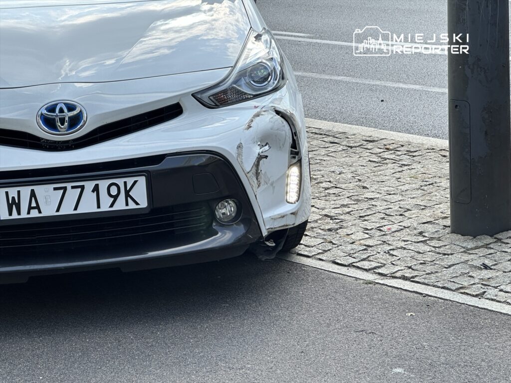 Uszkodzony srebrny samochód osobowy marki Toyota zaparkowany przy krawężniku na ulicy.