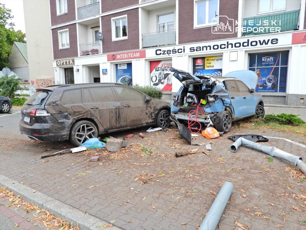 Dwa uszkodzone samochody zaparkowane na chodniku, obok sklepu z częściami samochodowymi, wśród porozrzucanych odpadków.