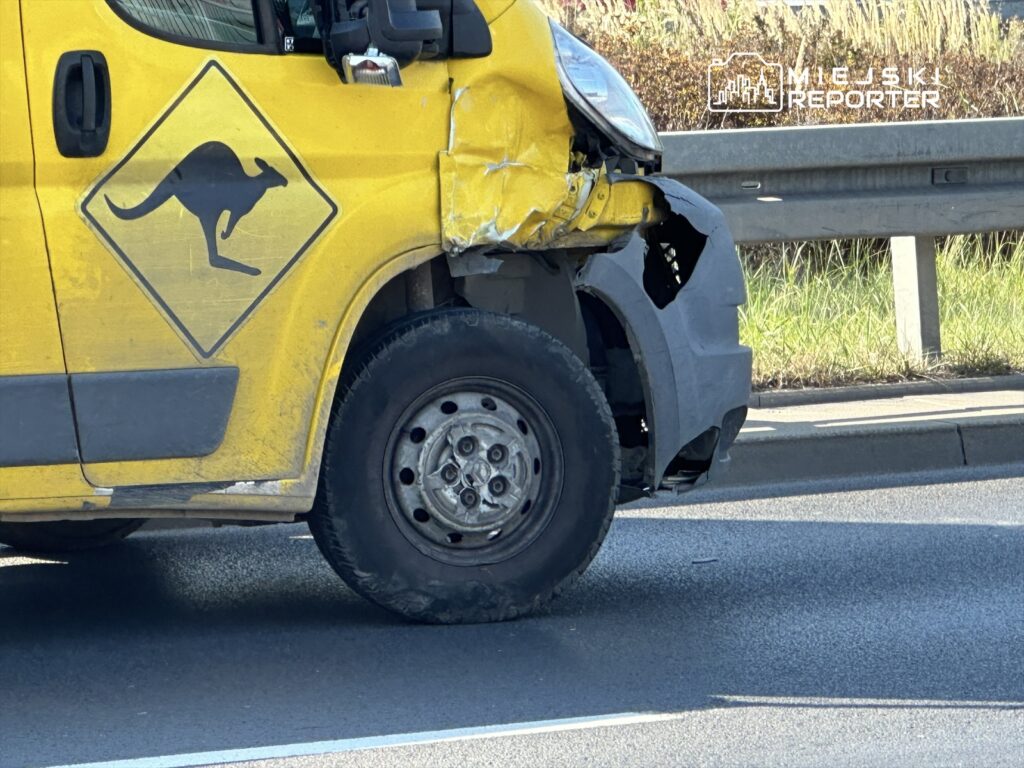 Uszkodzony żółty samochód dostawczy z logo kangura stojący na poboczu drogi.