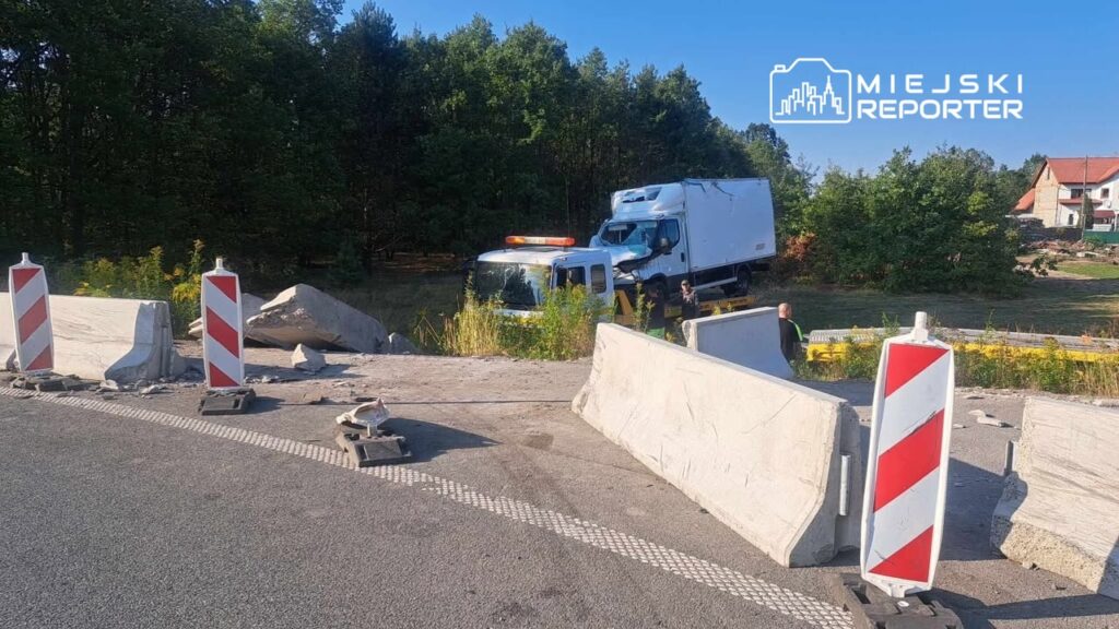 Ciężarówka utknęła przy barierkach na drodze, obok pracowników zabezpieczających teren w otoczeniu lasu.