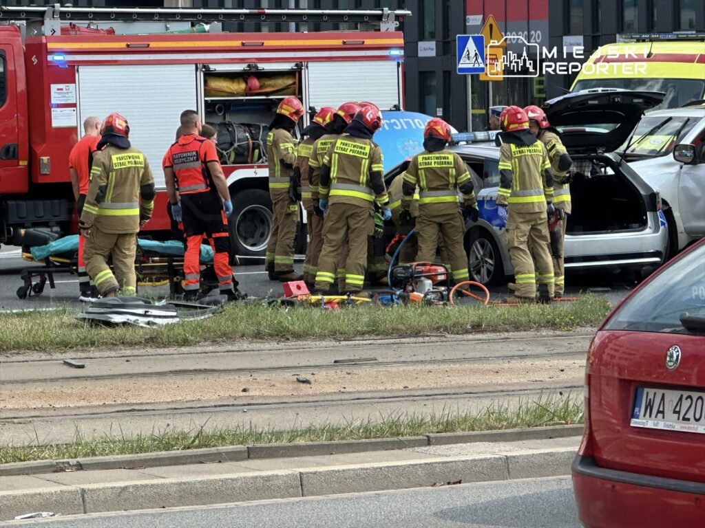 Grupa strażaków w mundurach ratunkowych pracuje przy wypadku drogowym, usuwając rozbite auto na ulicy.