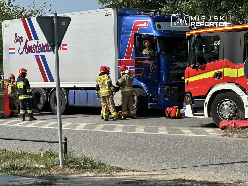 Grupa strażaków w mundurach prowadzi działania ratunkowe przy zderzeniu dwóch ciężarówek na skrzyżowaniu drogi.