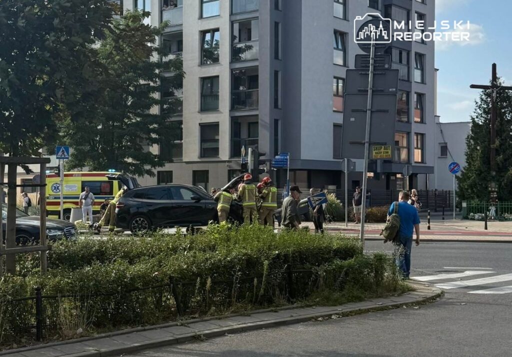 Grupa strażaków w mundurach pomaga przy usuwaniu zniszczeń po wypadku drogowym na ruchliwej ulicy.