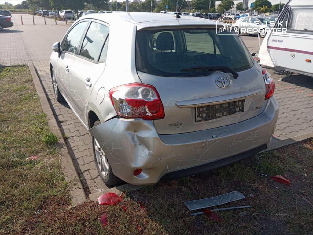 Uszkodzony srebrny samochód osobowy zaparkowany na parkingu, z widocznymi zarysowaniami i wgnieceniem z tyłu.