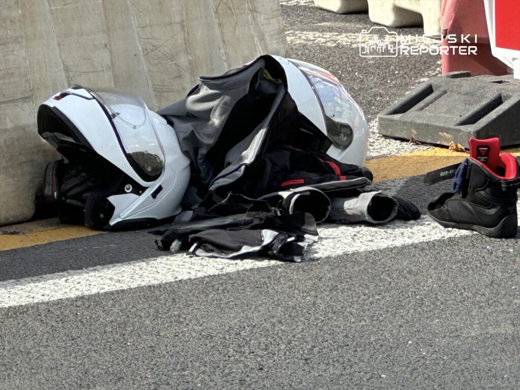 Kask motocyklowy i odzież ochronna leżą na jezdni obok barierki ochronnej.
