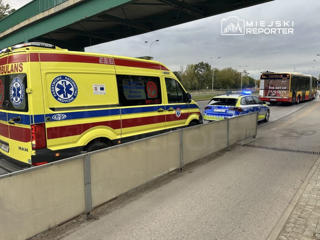 Karetka pogotowia oraz radiowóz policyjny zatrzymane na pasie drogowym, obok przejeżdżającego autobusu miejskiego.