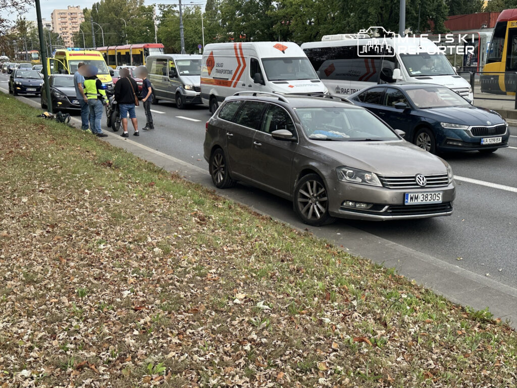 Grupa mężczyzn rozmawia obok motocykla na zatłoczonej ulicy, obok przejeżdżających pojazdów.