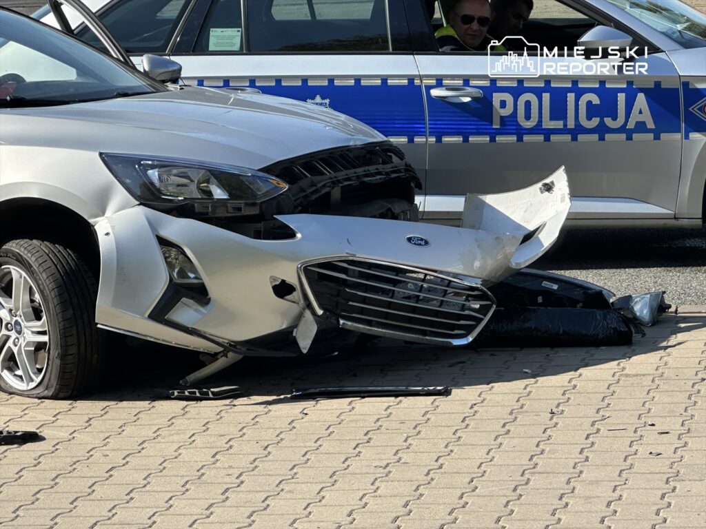 Uszkodzony samochód osobowy marki Ford z oderwaną przednią częścią, stojący obok radiowozu policji.