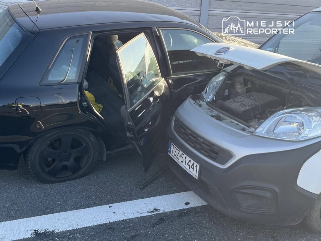 Czarne auto z otwartymi drzwiami stoi obok szarego samochodu z uniesioną maską na parkingu.