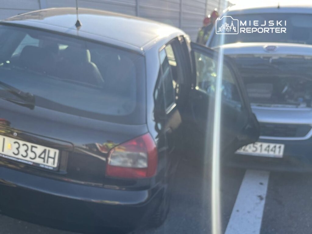 Czarny samochód osobowy z otwartymi drzwiami stoi obok niebieskiego pojazdu na parkingu.
