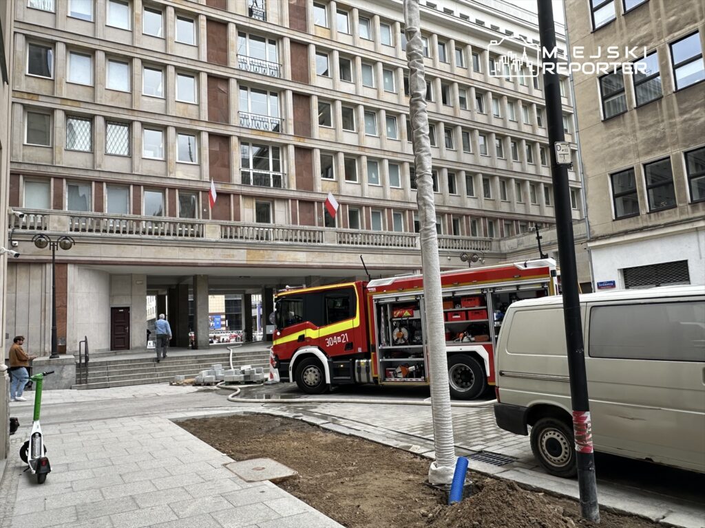 Straż pożarna z włączonymi sygnałami stoi przed nowoczesnym budynkiem w trakcie remontu.