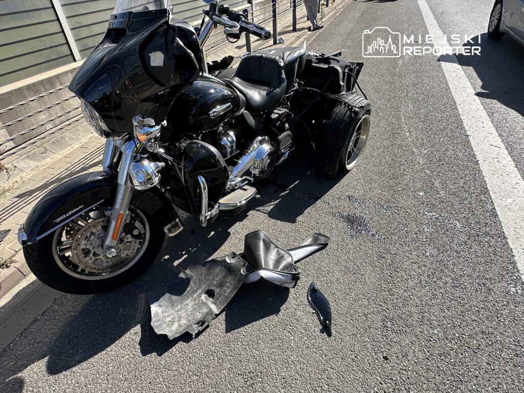 Motocykl w czarnym kolorze leży na drodze, obok znajdują się uszkodzone elementy pojazdu i plama oleju.
