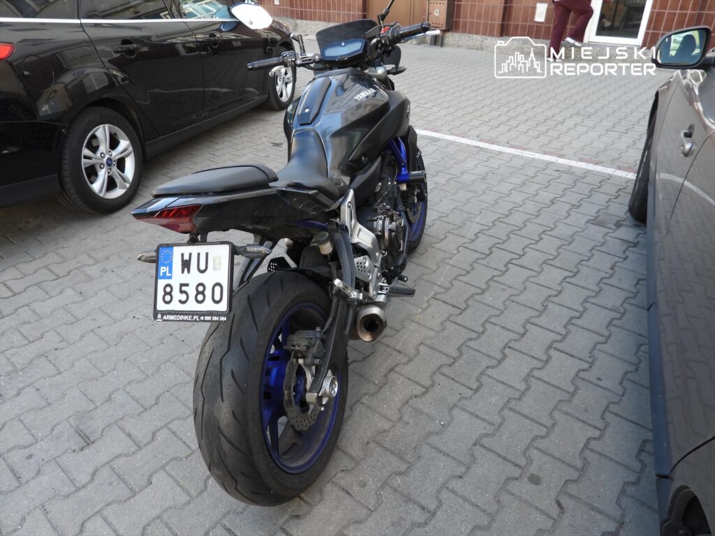 Motocykl sportowy w czarno-niebieskiej kolorystyce zaparkowany na placu z kostki brukowej między dwoma samochodami.