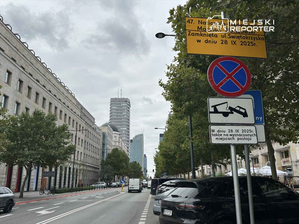 Ulica z nowoczesnymi budynkami, znak zakazu parkowania oraz tablica informująca o zamknięciu ul. Świętokrzyskiej 28 IX 2025 r.
