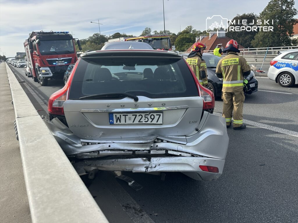 Uszkodzone volvo XC60 stoi na pasie ruchu, obok pracują strażacy w mundurach, a w tle widać zator drogowy.