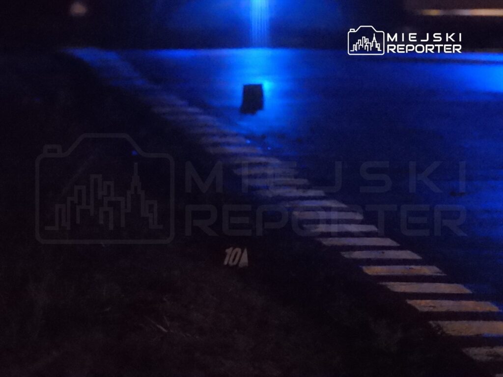 Na ciemnej ulicy widoczny znak z numerem 10A oraz niebieskie światła reflektorów.