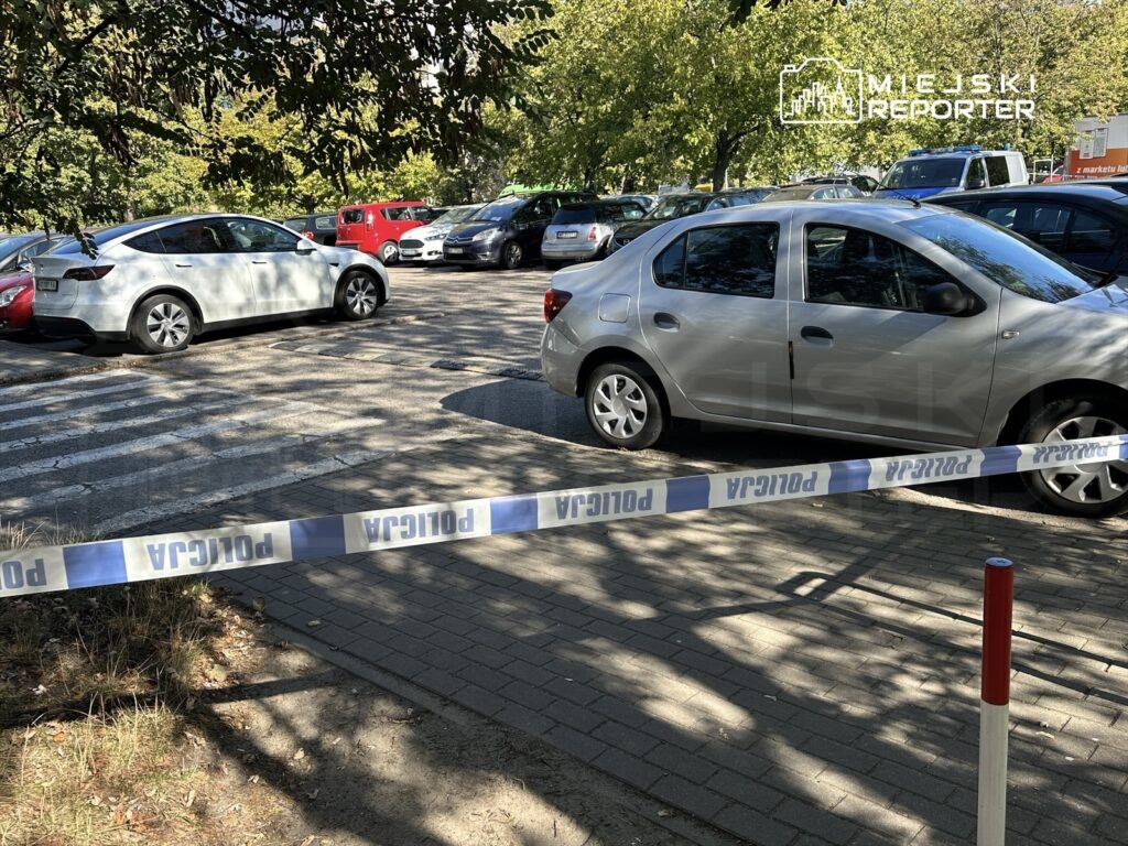 Na parkingu z widocznymi samochodami, białą taśmą policyjną oddzielono obszar, gdzie doszło do zdarzenia.