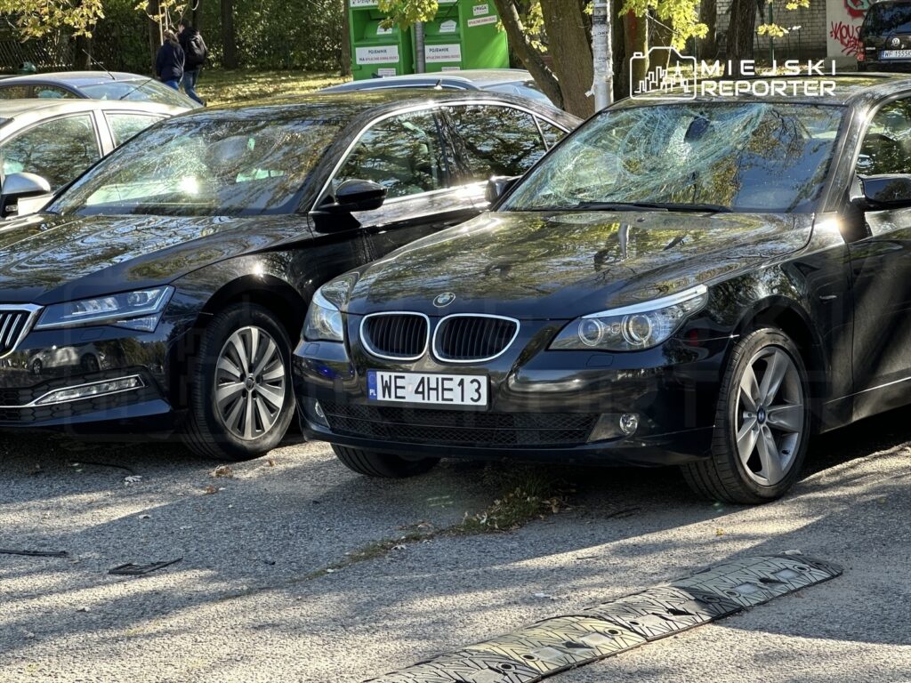 Dwa czarne samochody zaparkowane obok siebie na ulicy, w tle widać drzewa i przechodniów.