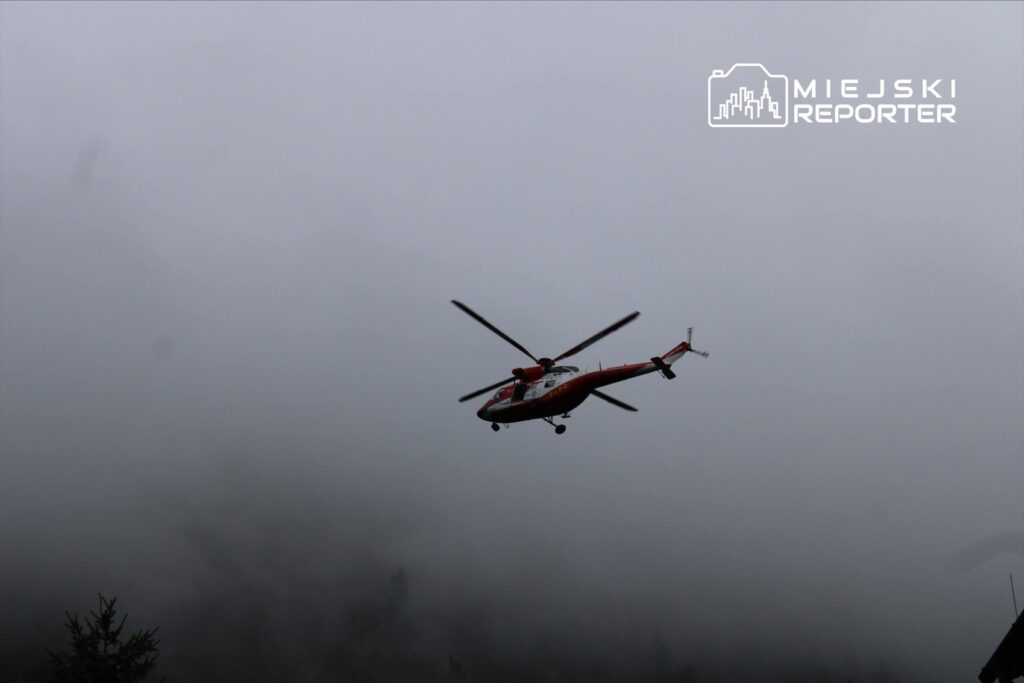 Czerwony helikopter przelatujący nad gęstą mgłą w górach.