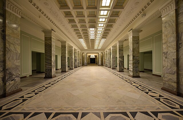 Przestronny hall z marmurowymi kolumnami, eleganckim oświetleniem i zdobioną posadzką.