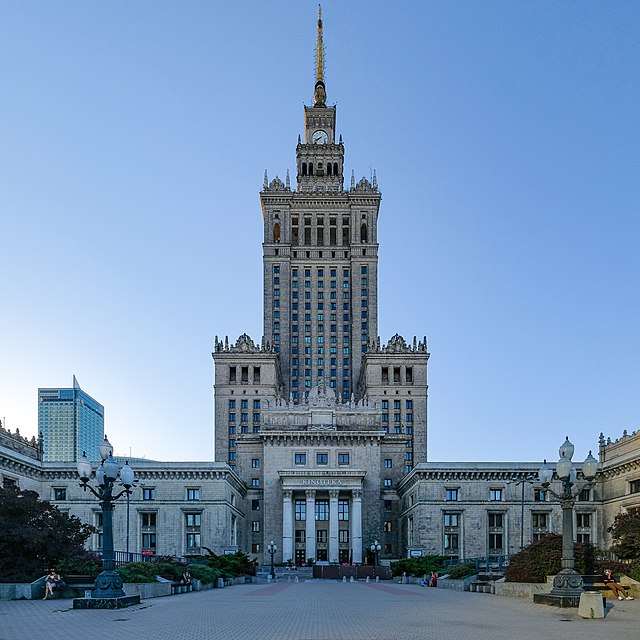 Wysoki, neoklasyczny budynek z wieżą i złotym szczytem, otoczony przestrzenią miejską i drzewami.